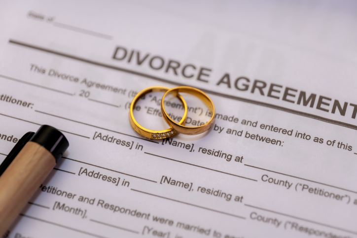 Golden wedding rings rest on a divorce agreement, symbolizing the end of a marriage.